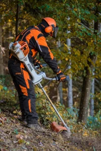 Lucrător cu echipament de protecție care curăță vegetația cu motocoasa